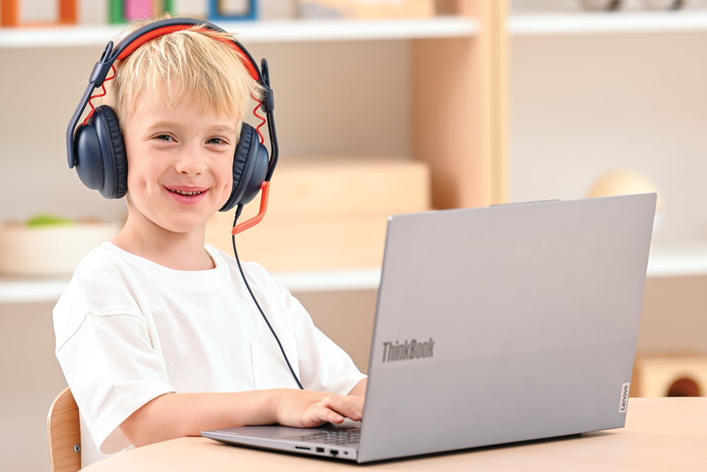 chłopiec iuczący się na laptopie Lenovo z słuchawkami na uszach